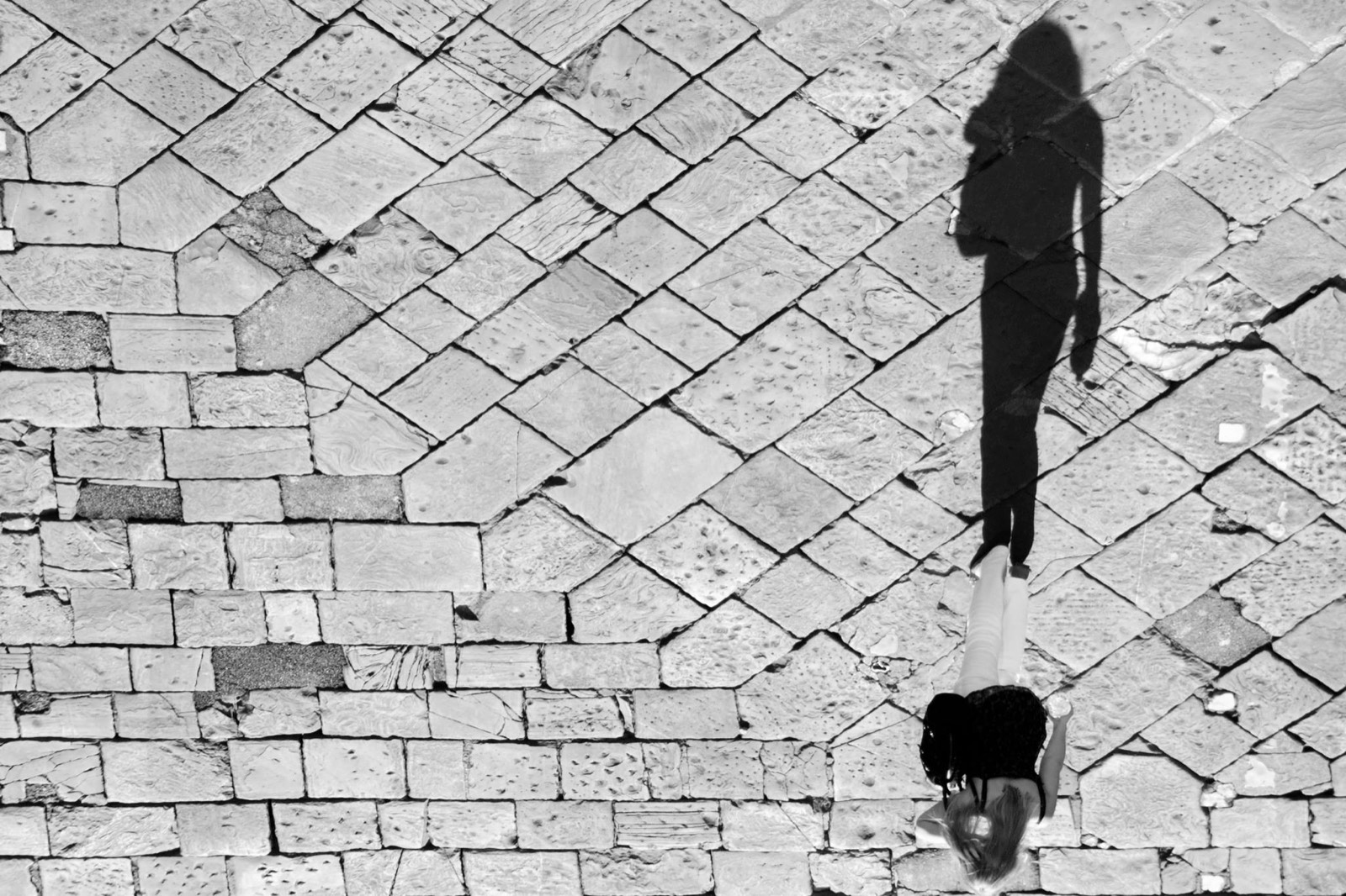 Ombra di una passante sul selciato, in bianco e nero