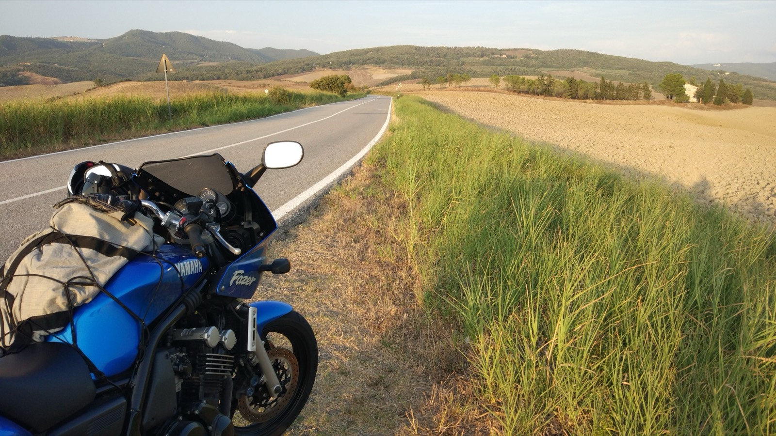 La moto ferma lungo una strada fra le colline toscane al tramonto